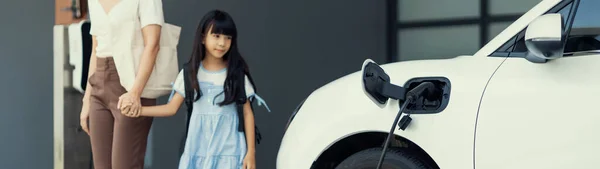 自宅で充電されている電気自動車で学校から戻ったばかりの母親と娘の進歩的なライフスタイル 持続可能なクリーンエネルギーを動力とする電気自動車 — ストック写真