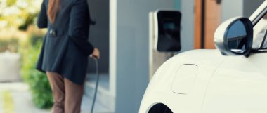 İlerici kadın elektrikli arabasının fişini şarj istasyonuna takıyor. İlerici bir yaşam tarzında elektrikli araç kullanımı kavramı temiz çevreye katkıda bulunur.