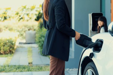Evde şarj edilen elektrikli bir araçla okuldan yeni dönen anne ve kızın ilerici yaşam tarzı. Elektrikli araç, sürdürülebilir temiz enerjiyle çalışıyor..
