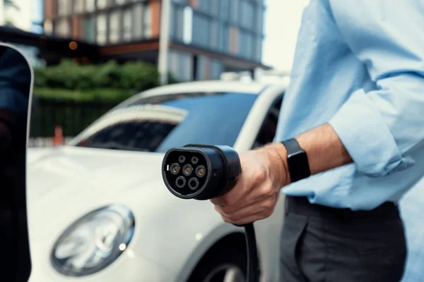 stock image Closeup progressive man holding EV charger plug from public charging station for electric vehicle with background of residential building as concept eco-friendly sustainability energy car concept.