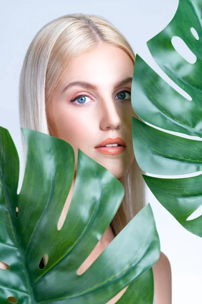 stock image Closeup facial portrait personable woman with perfect smooth makeup holding green monstera leaves and cover her face as natural healthy skincare treatment. Tropical nature and beauty concept