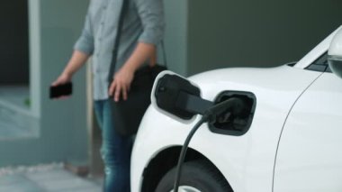 Adamın biri evinde elektrikli araç şarj aletinin fişini çekiyor. İlerici bir yaşam tarzında elektrikli araçların kullanımı, temiz ve sağlıklı bir çevreye katkıda bulunur..