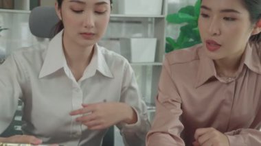 Ofis masasında çalışan iki hevesli genç iş kadını, veri tablosu raporlarıyla birlikte. Genç meslektaşlar istatistik veri kağıdı planları ve stratejisini tartışıyor ve analiz ediyorlar.