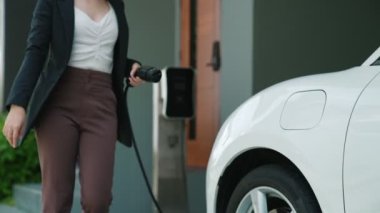 İlerici kadın evdeki elektrikli aracına şarj istasyonu fişi takıyor. EV otomobilleri çevreye yararlı temiz ve yeşil enerji kavramı sağlar.
