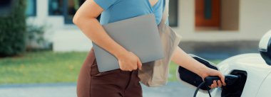 İlerici kadın elektrikli arabasının fişini şarj istasyonuna takıyor. İlerici bir yaşam tarzında elektrikli araç kullanımı kavramı temiz çevreye katkıda bulunur.