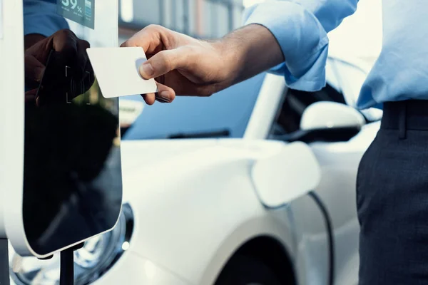 Hand holding credit card to pay public charging station and recharge her electric vehicle, symbolizing progressive lifestyle, combines e-wallet technology and sustainable transportation option.