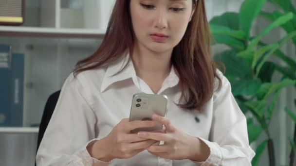 クライアントや同僚にスマートフォーンのテキストメッセージを使用してオフィスデスクで働く熱狂的な若いビジネスマンを閉じます アジアの女性従業員はプロの仕事のためのスマートフォンに夢中に — ストック動画