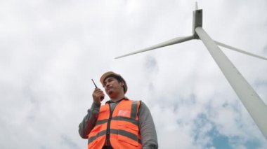 Gökyüzü arka planına sahip bir rüzgar türbini üzerinde çalışan mühendis. Yenilenebilir ve sürdürülebilir enerjinin gelecekteki üretimi için yenilikçi bir ideal. Rüzgar türbininden enerji üretimi.