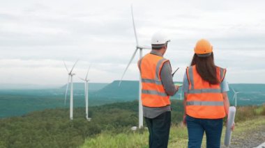 Erkek ve kadın mühendisler kırsal kesimdeki bir tepenin tepesinde ya da dağda rüzgar çiftliğinde çalışıyorlar. Yenilenebilir ve sürdürülebilir enerjinin gelecekteki üretimi için yenilikçi idealler.