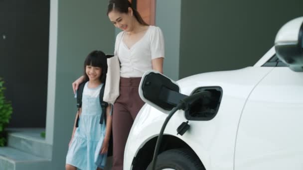 自宅で充電されている電気自動車で学校から戻ったばかりの母親と娘の進歩的なライフスタイル 持続可能なクリーンエネルギーを動力とする電気自動車 — ストック動画