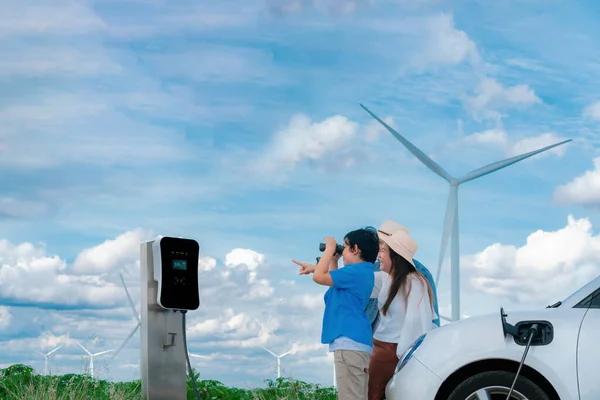 渐进式快乐家庭的概念 享受他们在风电场与电动汽车的时光 充电站风力涡轮机洁净可再生能源驱动的电动汽车 — 图库照片