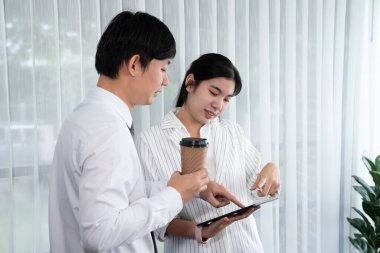 Manager advising guiding younger colleague with tablet in workplace. Couple businesspeople in formal wear working together on financial strategy as concept of teamwork and harmony in office.