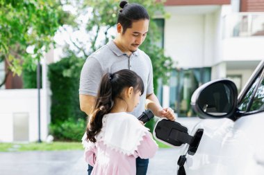 Progressive father and daughter returned from school in electric vehicle that is being charged at home. Electric vehicle driven by renewable clean energy. Home charging station concept for environment