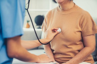 A contented retired senior woman being exterminated by her caregiver with a stethoscope at home. Medical care service, senior care at home.