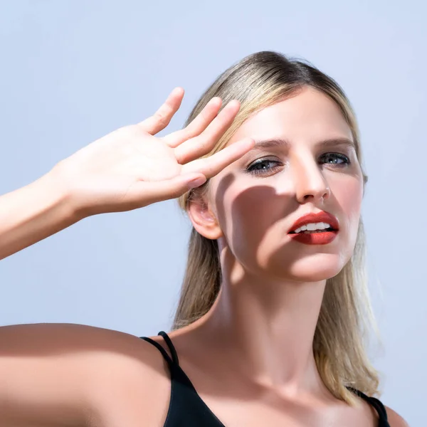 stock image Closeup young blond hair woman with perfect skin and soft alluring facial makeup raise her hand cover her face from bright sunlight in isolated background for skincare sunscreen product.