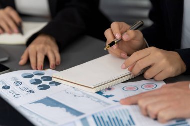 Closeup on BI dashboard on meeting desk with businesspeople analyzing or planning business strategy with hands pointing on financial paper reports as concept of harmony in office workplace.