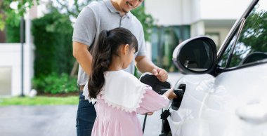 Progressive father and daughter returned from school in electric vehicle that is being charged at home. Electric vehicle driven by renewable clean energy. Home charging station concept for environment