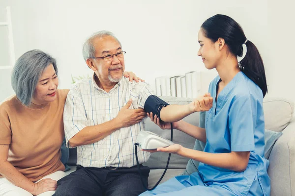 stock image An elderly man having a blood pressure check by his personal caregiver with his wife sitting next to him in their home.