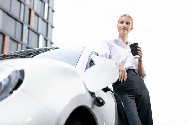 Businesswoman Drinking Coffee Leaning Electric Vehicle Recharging Public Charging Station — 图库照片