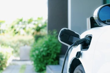 Closeup electric vehicle plugged-in with cable from charging point powered for progressive concept by alternative clean energy rechargeable EV car at home charging station.