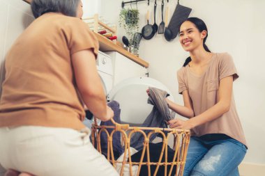 Daughter and mother working together to complete their household chores near the washing machine in a happy and contented manner. Mother and daughter doing the usual tasks in the house.