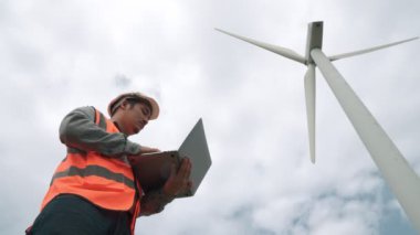 Gökyüzü arka planına sahip bir rüzgar türbini üzerinde çalışan mühendis. Yenilenebilir ve sürdürülebilir enerjinin gelecekteki üretimi için yenilikçi bir ideal. Rüzgar türbininden enerji üretimi.