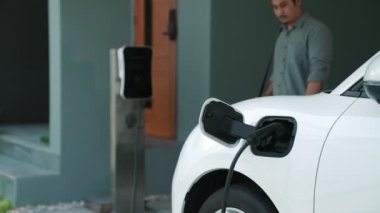 Adamın biri evinde elektrikli araç şarj aletinin fişini çekiyor. İlerici bir yaşam tarzında elektrikli araçların kullanımı, temiz ve sağlıklı bir çevreye katkıda bulunur..