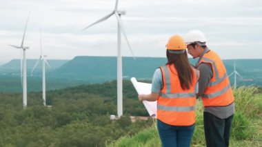 Erkek ve kadın mühendisler kırsal kesimdeki bir tepenin tepesinde ya da dağda rüzgar çiftliğinde çalışıyorlar. Yenilenebilir ve sürdürülebilir enerjinin gelecekteki üretimi için yenilikçi idealler.