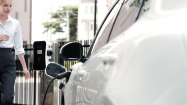 İlerici iş kadını, şehir merkezinde dolaşmadan önce şarj cihazının fişini şarj istasyonundan elektrikli arabasına çekti. Çevre dostu şarj edilebilir araba, sürdürülebilir ve temiz enerjiyle çalışıyor..