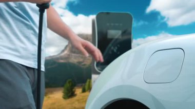 İlerici adam şarj noktasında elektrikli araba yüklüyor, daha temiz bir çevre için temiz ve yenilenebilir enerjiyle çalışan bir EV ile doğada ve dağlarda seyahat ediyor..