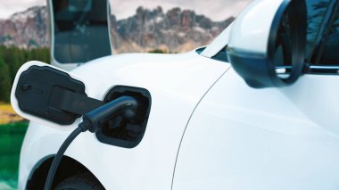 Elektro jeneratör sürücüsüyle enerji sürdürülebilir araba gücü, şarj istasyonunda şarj edilen batarya, ilerici seyahat konsepti için dağ zeminine sahip. Temiz ortamın sembolü olarak doğadaki EV otomobil.
