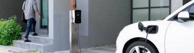 Progressive asian man and electric car with home charging station. Concept of the use of electric vehicles in a progressive lifestyle contributes to a clean and healthy environment.