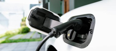 Closeup electric vehicle plugged-in with cable from charging point powered for progressive concept by alternative clean energy rechargeable EV car at home charging station.