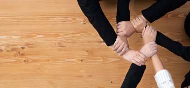 Top view partial hands wearing formal suit joining stack and form circle as symbol of team building, unity and harmony in office workplace. Successful business team of synergy holding hand together.