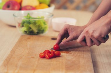 Close up hands holding a knife preparing a contented meal. Sliced tomatoes and other vegetables on the glass dish.