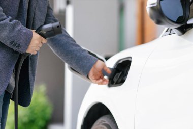 Closeup progressive asian man install cable plug to his electric car with home charging station. Concept of the use of electric vehicles in a progressive lifestyle contributes to clean environment.