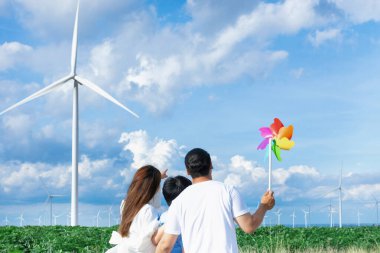 İlerici mutlu aile kavramı rüzgâr türbini çiftliğinde eğleniyor. Rüzgar türbini jeneratörüyle gelen elektrik jeneratörü kırsal bölgede tepe ve ufukta dağ var..
