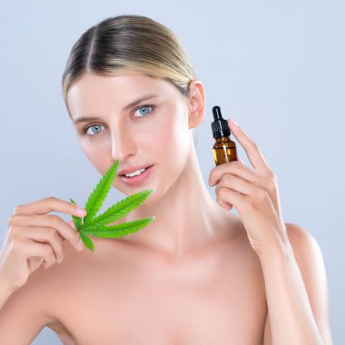Alluring portrait of beautiful woman in isolated holding green leaf with marijuan extracted bottle for skincare treatment product. Cannabis CBD oil for cosmetology and beauty concept.