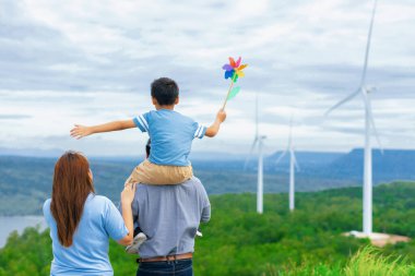 Progressive happy family enjoying their time at wind farm for green energy production concept. Wind turbine generators provide clean renewable energy for eco-friendly purposes.