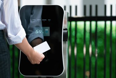 Hand holding credit card to pay public charging station and recharge her electric vehicle, symbolizing progressive lifestyle, combines e-wallet technology and sustainable transportation option.