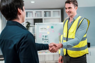 An engineer with a protective vest handshake with an investor in his office. Following a successful meeting, employee and employer form a partnership.