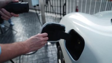 İlerici işadamı, şehir merkezinde dolaşmadan önce şarj cihazından elektrikli arabasına şarj prizi takıyor. Çevre dostu şarj edilebilir araba, sürdürülebilir ve temiz enerjiyle çalışıyor..