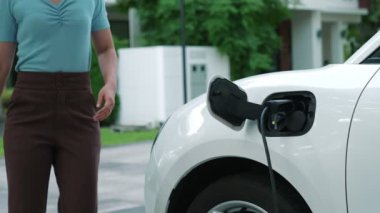 Bir kadın evinde elektrikli araç şarj aletinin fişini çekiyor. İlerici bir yaşam tarzında elektrikli araçların kullanımı, temiz ve sağlıklı bir çevreye katkıda bulunur..