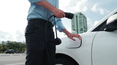 İlerici işadamı, şehir merkezinde dolaşmadan önce şarj cihazından elektrikli arabasına şarj prizi takıyor. Çevre dostu şarj edilebilir araba, sürdürülebilir ve temiz enerjiyle çalışıyor..