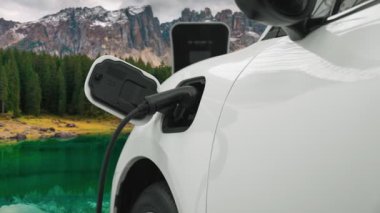 Temiz çevre için temiz enerjinin yol açtığı ilerici elektrikli araba kavramının arka planı olarak dağın tepesinde bulutun zaman kavramının yer aldığı doğal manzara. EV araba şarj istasyonunda şarj oluyor..