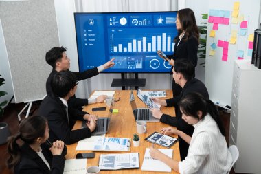 Confidence and young asian businesswoman give presentation on financial business strategy in dashboard report display on screen to colleagues in conference room meeting as harmony in workplace concept