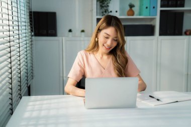 A young Asian female employee sitting at her desk in her office, sitting at desktop in workstation.