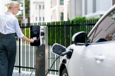 Credit card payment for eco-friendly clean and sustainable energy for electric vehicle at charging station. Progressive woman pay for charging point to power his electric rechargeable vehicle.