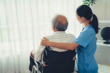 Rear view of a caregiver and her contented senior patient gazing out through the window. Elderly illness, nursing homes for the elderly, and pensioner life