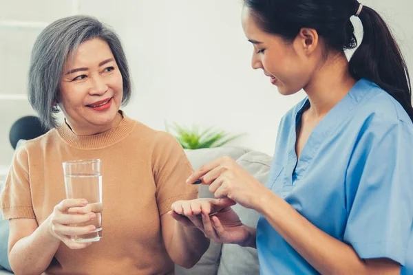 Contented senior woman taking medicines while her caregiver advising her medication. Medication for seniors, nursing house, healthcare at home.